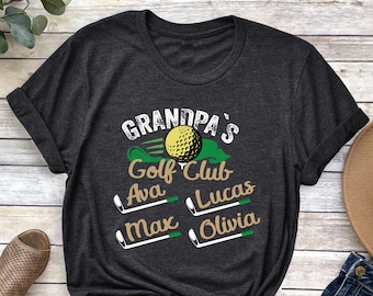 Può includere: Una maglietta grigia scura con il testo "Grandpa's Golf Club" e i nomi Ava, Lucas, Max e Olivia stampati su di essa. La maglietta ha una grafica di campo da golf verde e palla da golf.