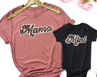 May include: A set of two shirts, one pink and one black, with the words "Mama" and "Mini" in a leopard print font.