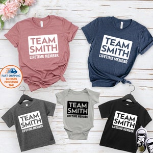 May include: Four shirts with the text "Team Smith Lifetime Member" in a white rectangle. The shirts are in different colors: pink, blue, gray, and black. There is also a gray baby onesie with the same text.