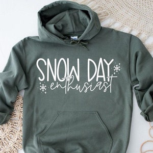 May include: A green hooded sweatshirt with the text "SNOW DAY enthusiast" in white lettering and a snowflake graphic.