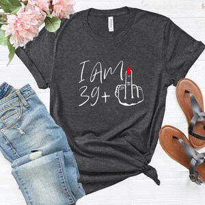 May include: A dark gray t-shirt with the text "I AM 39+" and a white hand with a red fingernail giving the middle finger.