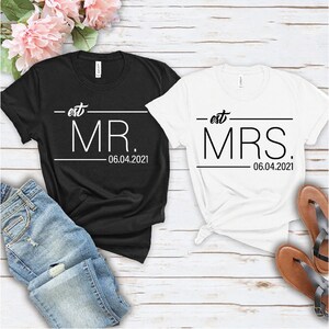May include: Two black and white t-shirts with the text "est. MR. 06.04.2021" and "est. MRS. 06.04.2021" printed on them.