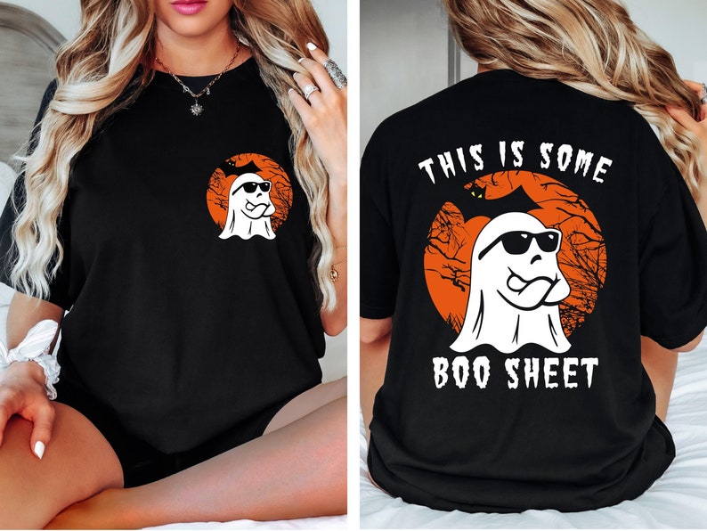 May include: Black t-shirt featuring a white ghost wearing sunglasses, set against an orange circle with a tree silhouette. The back of the shirt has the text "THIS IS SOME BOO SHEET". A fun Halloween-themed graphic tee.