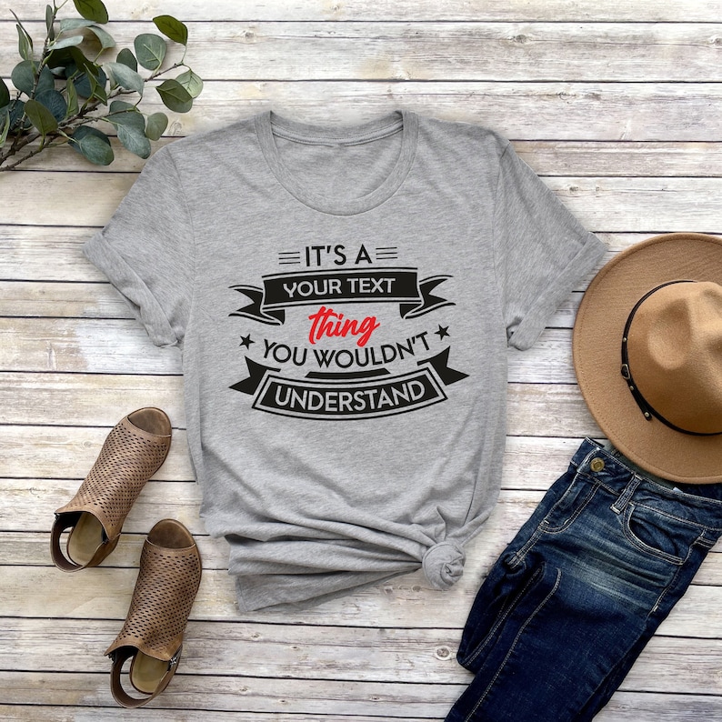 K&ouml;nnte beinhalten: Graues T-Shirt mit schwarzem Text, der "It's a your text thing you wouldn't understand" lautet. Der Text befindet sich auf einem schwarzen Banner mit wei&szlig;en Sternen.