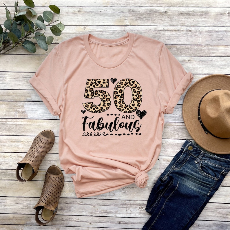 Puede incluir: Una camiseta rosa con un dise&ntilde;o de estampado de leopardo con el n&uacute;mero 50 y el texto "and Fabulous".