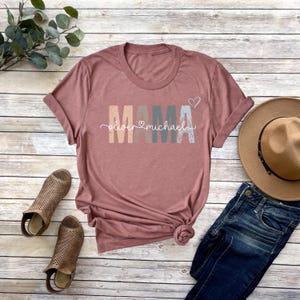 May include: A mauve colored t-shirt with the word "MAMA" in colorful block letters and the text "oliver &hearts; michael" underneath.
