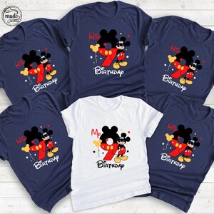 Op de afbeelding: Een verzameling marineblauwe en witte t-shirts met een Mickey Mouse-afbeelding. Het ontwerp bevat een groot rood nummer 9, het woord "Birthday" en de zinnen "His" en "My". De shirts hebben korte mouwen en een ronde hals.