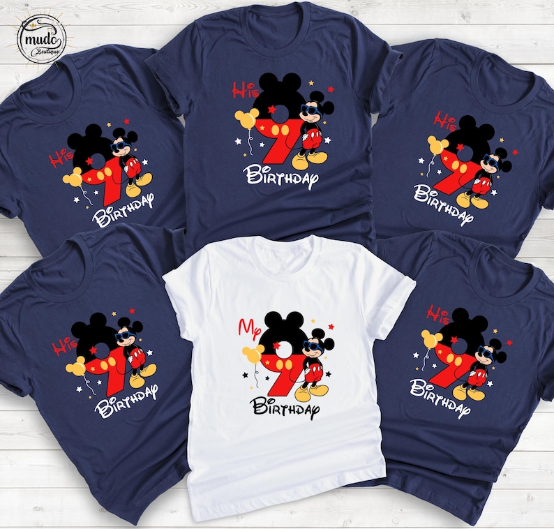 Op de afbeelding: Een verzameling marineblauwe en witte t-shirts met een Mickey Mouse-afbeelding. Het ontwerp bevat een groot rood nummer 9, het woord "Birthday" en de zinnen "His" en "My". De shirts hebben korte mouwen en een ronde hals.