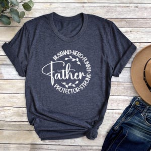 May include: A dark blue t-shirt with a white circle graphic that says "Father" with the words "Husband, Hero, Funny, Protector, Strong" around the circle.