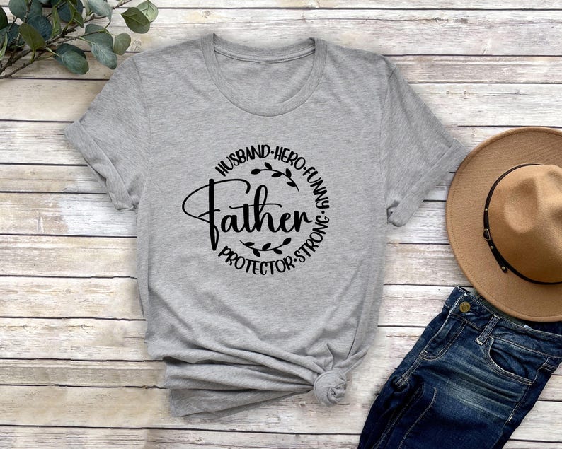 May include: Grey t-shirt with a black circle design that says "Husband, Hero, Funny, Father, Protector, Strong".