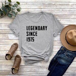 May include: Gray t-shirt with black text that reads "Legendary Since 1975".