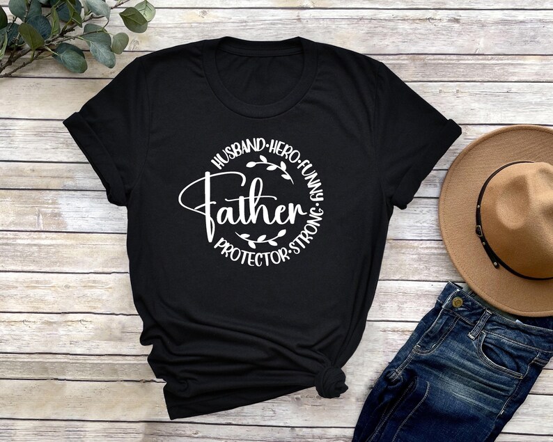 May include: Black t-shirt with a white circle graphic that says "Husband, Hero, Funny, Father, Protector, Strong".