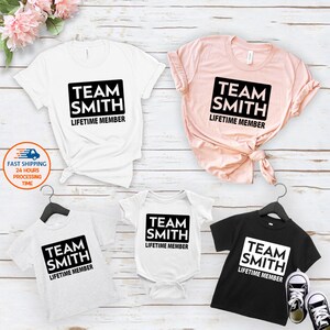 May include: A set of four t-shirts with the text "Team Smith Lifetime Member" in a black rectangle on each shirt. The shirts are in different colors: white, pink, gray, and black.