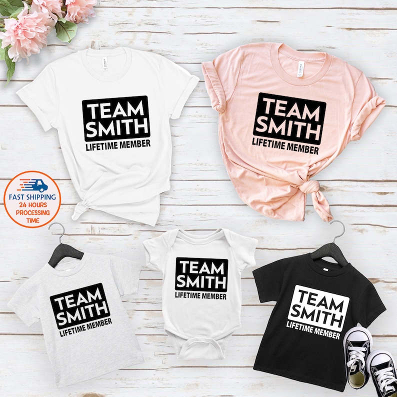 May include: A set of four t-shirts with the text "Team Smith Lifetime Member" in a black rectangle on each shirt. The shirts are in different colors: white, pink, gray, and black.