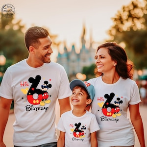 Op de afbeelding: Witte T-shirts met een Mickey Mouse-ontwerp, met de tekst "His Birthday" en "My Birthday". Het ontwerp bevat een groot cijfer 6, Mickey Mouse en kleurrijke accenten. De familie lacht.