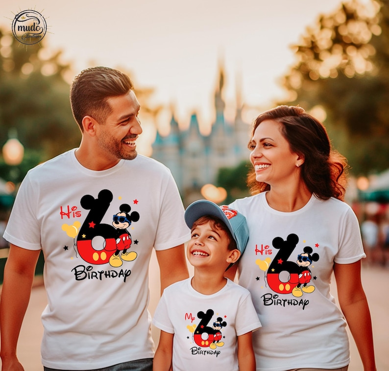 Op de afbeelding: Witte T-shirts met een Mickey Mouse-ontwerp, met de tekst "His Birthday" en "My Birthday". Het ontwerp bevat een groot cijfer 6, Mickey Mouse en kleurrijke accenten. De familie lacht.