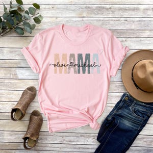 May include: Pink t-shirt with the word "MAMA" in rainbow colors and the names "Oliver" and "Michael" written below.