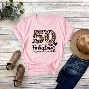 Puede incluir: Camiseta rosa con un dise&ntilde;o de estampado de leopardo con el n&uacute;mero 50 y el texto "AND Fabulous".