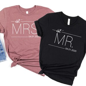 May include: Two t-shirts, one in a dusty rose color and one in black, with the text "est. MRS. 04.01.2020" and "est. MR. 04.01.2020" printed in white.