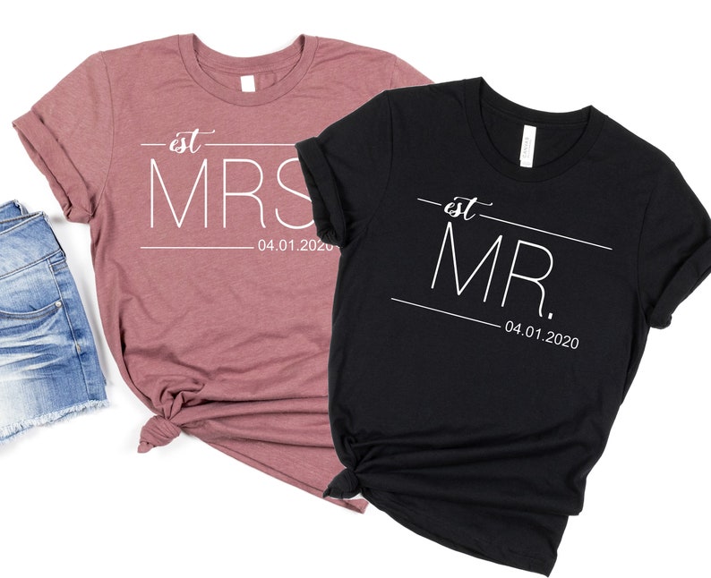 May include: Two t-shirts, one in a dusty rose color and one in black, with the text "est. MRS. 04.01.2020" and "est. MR. 04.01.2020" printed in white.