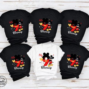Op de afbeelding: Zwarte en witte T-shirts met een Mickey Mouse-ontwerp. Het ontwerp bevat een groot rood nummer 7, Mickey Mouse en de woorden "His Birthday" of "My Birthday". De shirts zijn korte mouwen.