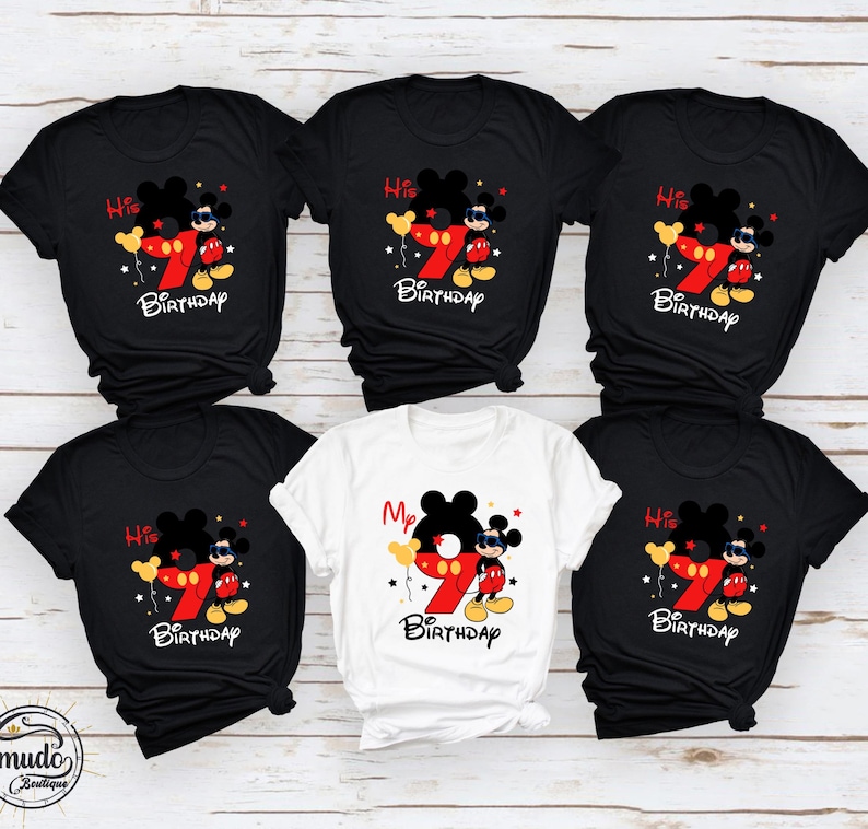 Op de afbeelding: Zwarte en witte T-shirts met een Mickey Mouse-ontwerp. Het ontwerp bevat een groot rood nummer 7, Mickey Mouse en de woorden "His Birthday" of "My Birthday". De shirts zijn korte mouwen.