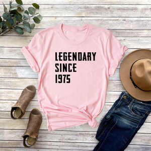 May include: Pink t-shirt with black text that reads "Legendary Since 1975".