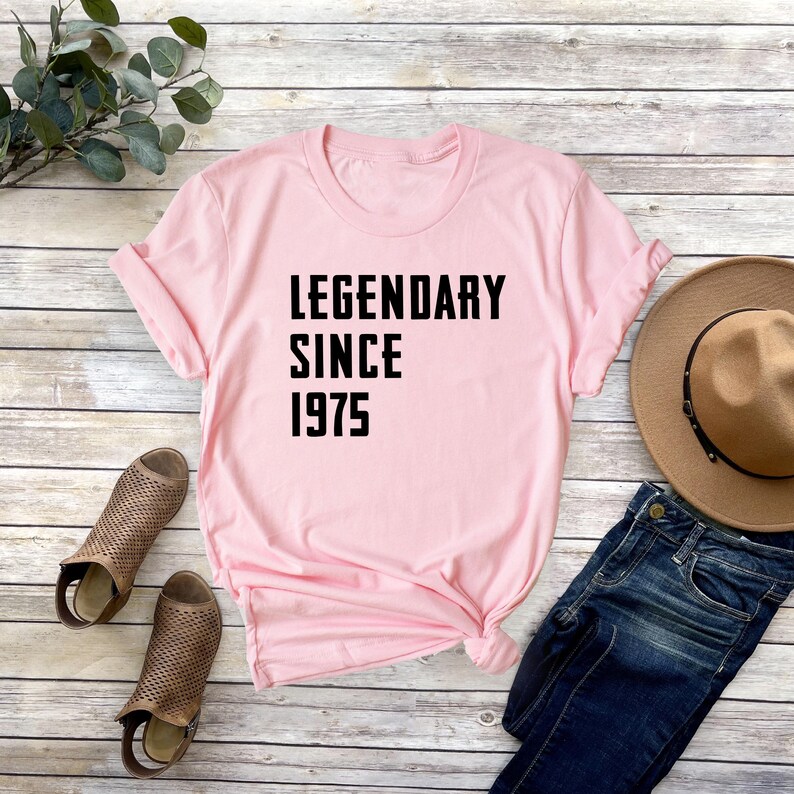 May include: Pink t-shirt with black text that reads "Legendary Since 1975".