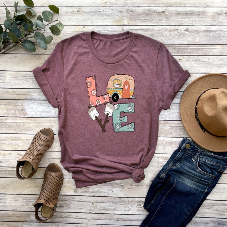 May include: A maroon t-shirt with a graphic of the word "LOVE" with a camper van and marshmallows. The letters are made of different patterns and colors.