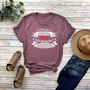 K&ouml;nnte beinhalten: Ein maroonfarbenes T-Shirt mit wei&szlig;em Text, der "It's a personal thing you wouldn't understand" lautet. Der Text ist in einem Banner-Stil mit Sternen auf beiden Seiten.