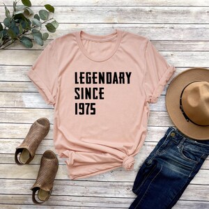 May include: A light pink t-shirt with black text that reads "LEGENDARY SINCE 1975".