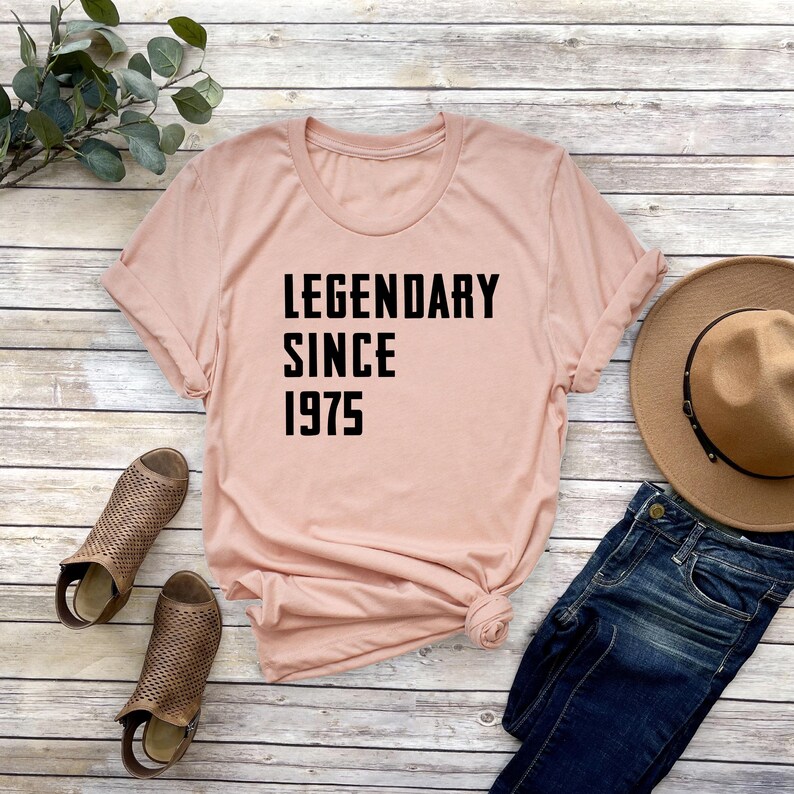May include: A light pink t-shirt with black text that reads "LEGENDARY SINCE 1975".