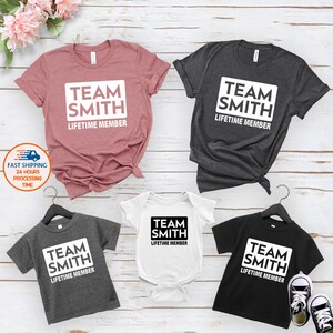 May include: Four t-shirts with the text "Team Smith Lifetime Member" in a white box. The shirts are in different colors: pink, gray, white, and black. The shirts are arranged in a grid pattern.