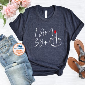 May include: A dark blue t-shirt with white text that reads "I AM 39+" and a white hand giving the middle finger with a red fingernail.