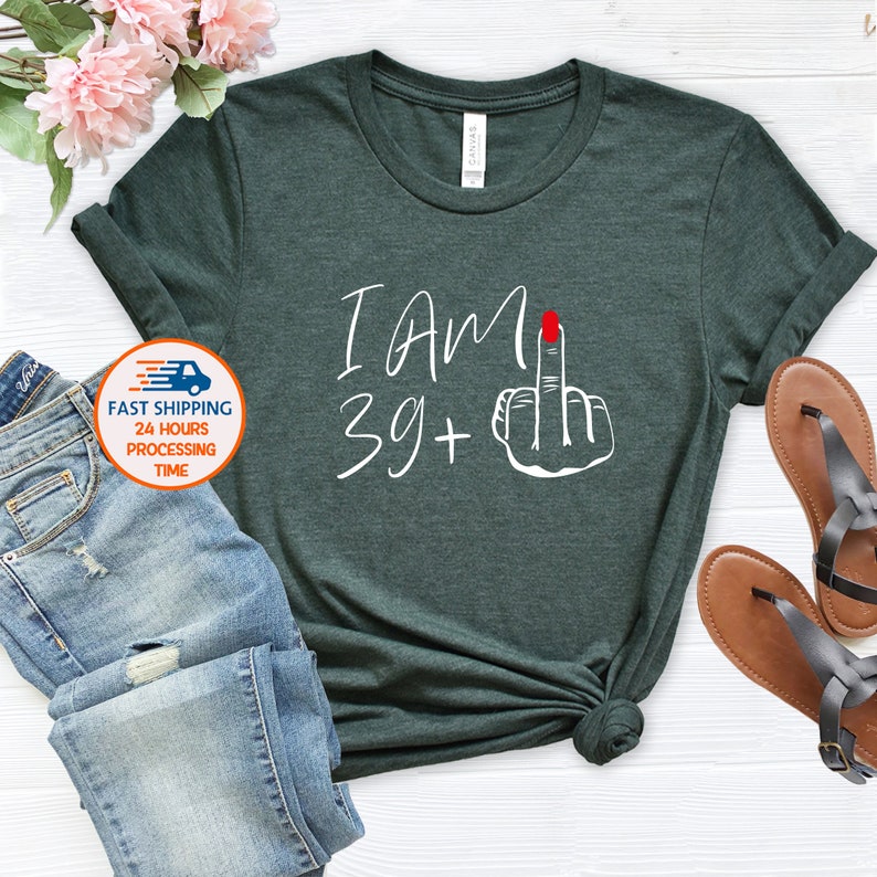 May include: A dark green t-shirt with white text that says "I am 39+" and a white illustration of a middle finger with a red nail.