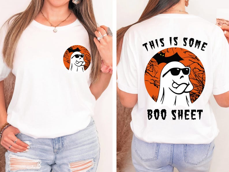 May include: White t-shirt featuring a Halloween-themed design. The front has a small circular graphic of a ghost wearing sunglasses. The back of the shirt has a larger graphic with the text "THIS IS SOME BOO SHEET".