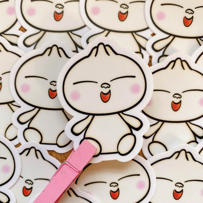 May include: A collection of white cartoon character stickers with closed eyes and smiling mouths. The characters have rosy cheeks and are shaped like a bun. The stickers are arranged in a random pattern on a brown surface.