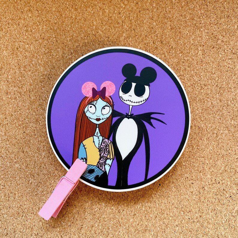 May include: A purple circle sticker with a cartoon image of Jack Skellington and Sally from the Nightmare Before Christmas. Jack is wearing a black and white suit and Sally is wearing a pink bow and a blue and yellow dress.