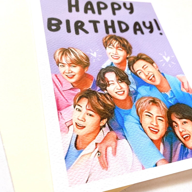 Pode incluir: Um cart&atilde;o roxo com o texto "Happy Birthday!" em letras pretas. Um grupo de sete homens &eacute; retratado no cart&atilde;o, sorrindo e olhando para a c&acirc;mera. Os homens est&atilde;o vestindo camisas de v&aacute;rias cores e est&atilde;o dispostos em um abra&ccedil;o em grupo.