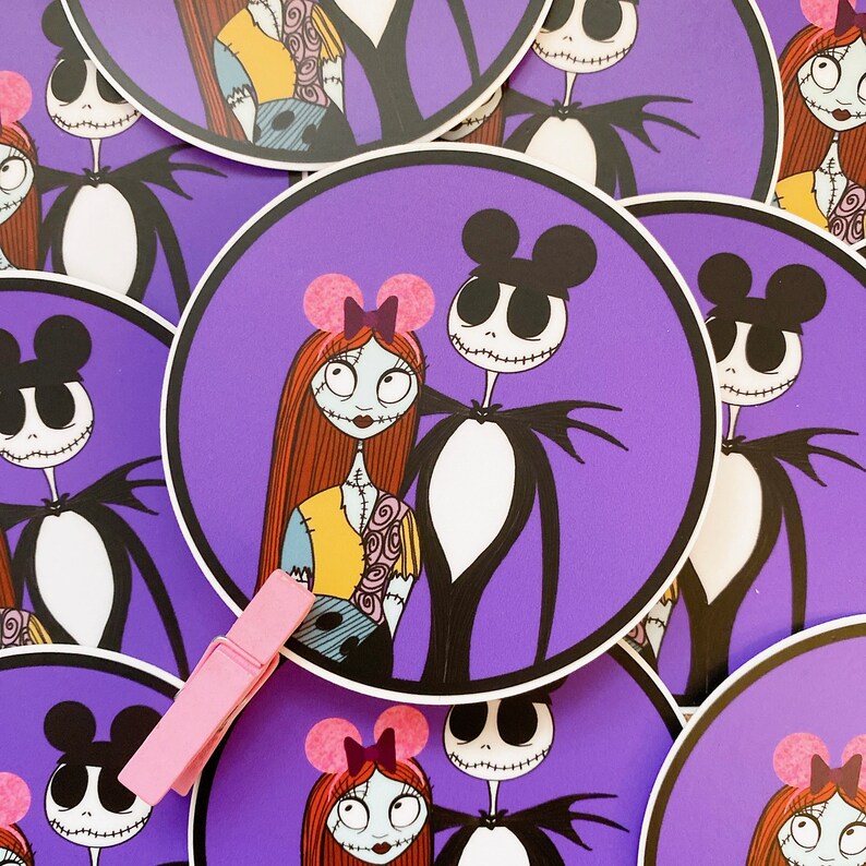 May include: A set of round stickers featuring a purple background with a black and white illustration of Jack Skellington and Sally from the Nightmare Before Christmas movie. Sally is wearing a pink bow and Mickey Mouse ears.