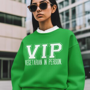 May include: A green sweatshirt with the text "VIP VEGETARIAN IN PERSON" in white. The person in the image is wearing sunglasses and a white collared shirt underneath the sweatshirt.