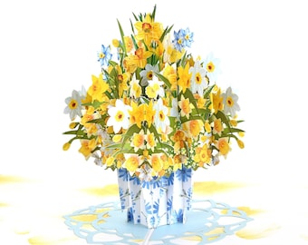 May include: A 3D pop-up card featuring a bouquet of yellow and white daffodils in a blue and white patterned vase. The card is open and the flowers are in focus.