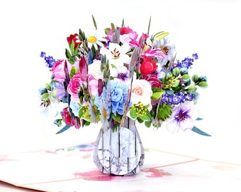May include: A 3D pop-up card featuring a vibrant bouquet of paper flowers. The arrangement includes pink roses, white lilies, blue hydrangeas, and purple blooms, all set in a gray vase. The card is open, revealing the intricate floral design.