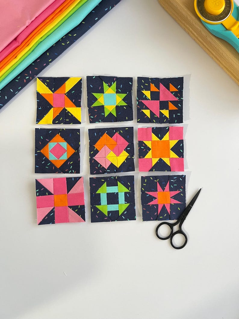 Peut inclure: Neuf blocs de courtepointe en tissu carr&eacute;s dispos&eacute;s en grille, chacun pr&eacute;sentant un fond bleu marine fonc&eacute; avec un motif de confettis et des formes g&eacute;om&eacute;triques aux couleurs vives rose, orange, jaune et bleu clair. Des ciseaux noirs sont pos&eacute;s.