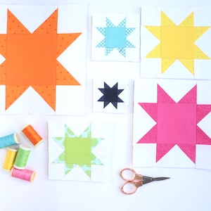 Pode incluir: Uma coleção de blocos de colcha de estrelas coloridas em laranja, azul, amarelo, preto, rosa e verde. Os blocos estão em quadrados brancos, com carretéis de linha e tesouras por perto. Os blocos de estrelas são um projeto de artesanato.