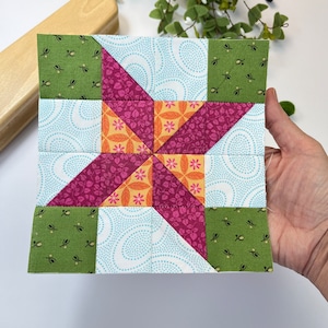 Op de afbeelding: Een patchwork quiltblok met een stervormig ontwerp. Het blok is gemaakt van negen vierkanten, elk met een ander patroon. De vierkanten zijn in tinten groen, roze, oranje en blauw.