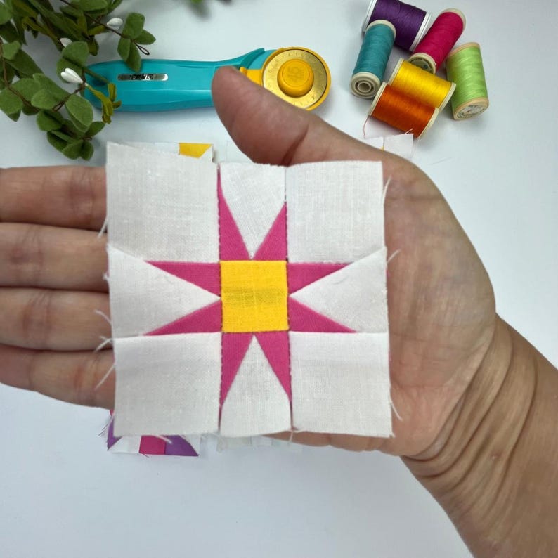Peut inclure: Un bloc de courtepointe en tissu carr&eacute; pr&eacute;sentant un carr&eacute; central jaune entour&eacute; d'une &eacute;toile rose &agrave; huit branches sur un fond blanc. Le bloc est compos&eacute; de pi&egrave;ces de tissu blanches, roses et jaunes assembl&eacute;es en un motif g&eacute;om&eacute;trique en &eacute;toile.