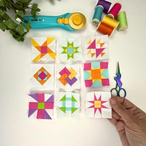 Peut inclure: Neuf blocs de courtepointe en tissu carr&eacute; pr&eacute;sentant des motifs g&eacute;om&eacute;triques aux couleurs vives, notamment rose, orange, jaune, violet et bleu sarcelle. L'ensemble comprend un cutter rotatif, des bobines de fil et des ciseaux iris&eacute;s.
