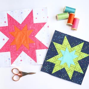 Pode incluir: Dois blocos de colcha em estrela coloridos, um rosa e laranja, o outro azul e verde, estão em uma superfície branca. Pequenos carretéis de linha em várias cores e um par de tesouras douradas também estão presentes. Os blocos são para um projeto de quilting.