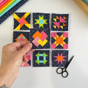 Peut inclure: Une collection de neuf blocs de courtepointe en tissu carr&eacute; dispos&eacute;s en grille. Chaque bloc pr&eacute;sente un fond bleu marine fonc&eacute; avec un imprim&eacute; confettis et des motifs g&eacute;om&eacute;triques en tissus jaune vif, orange, rose et bleu clair.